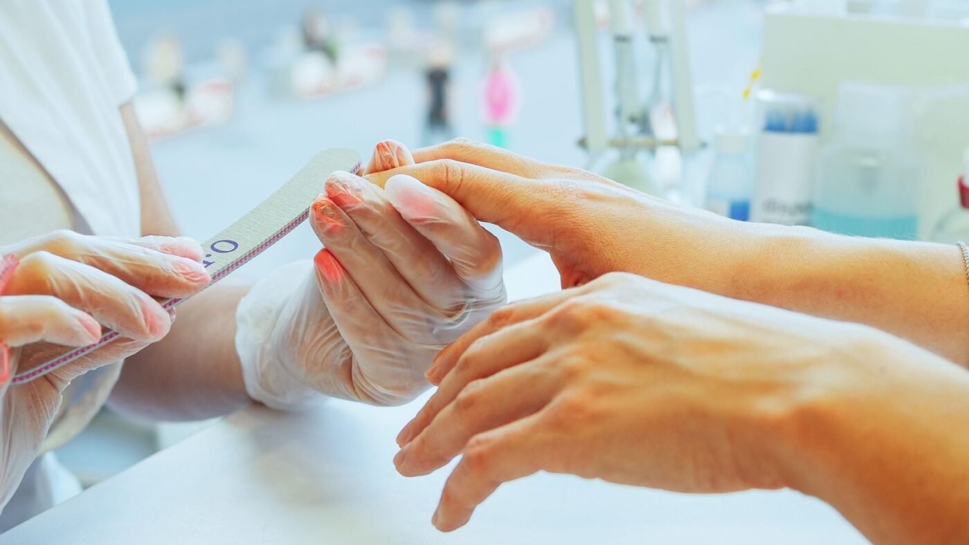 Manicure de luvas lixando as unhas de uma cliente em mesa de salão