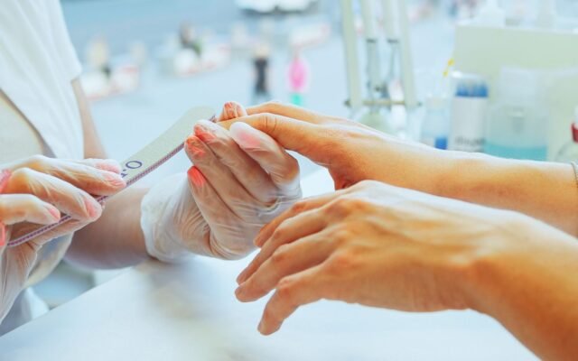 Manicure de luvas lixando as unhas de uma cliente em mesa de salão