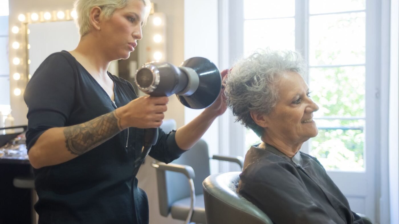 Cabeleireira secando com secador o cabelo de uma cliente idosa no salão de beleza