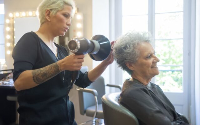 Cabeleireira secando com secador o cabelo de uma cliente idosa no salão de beleza