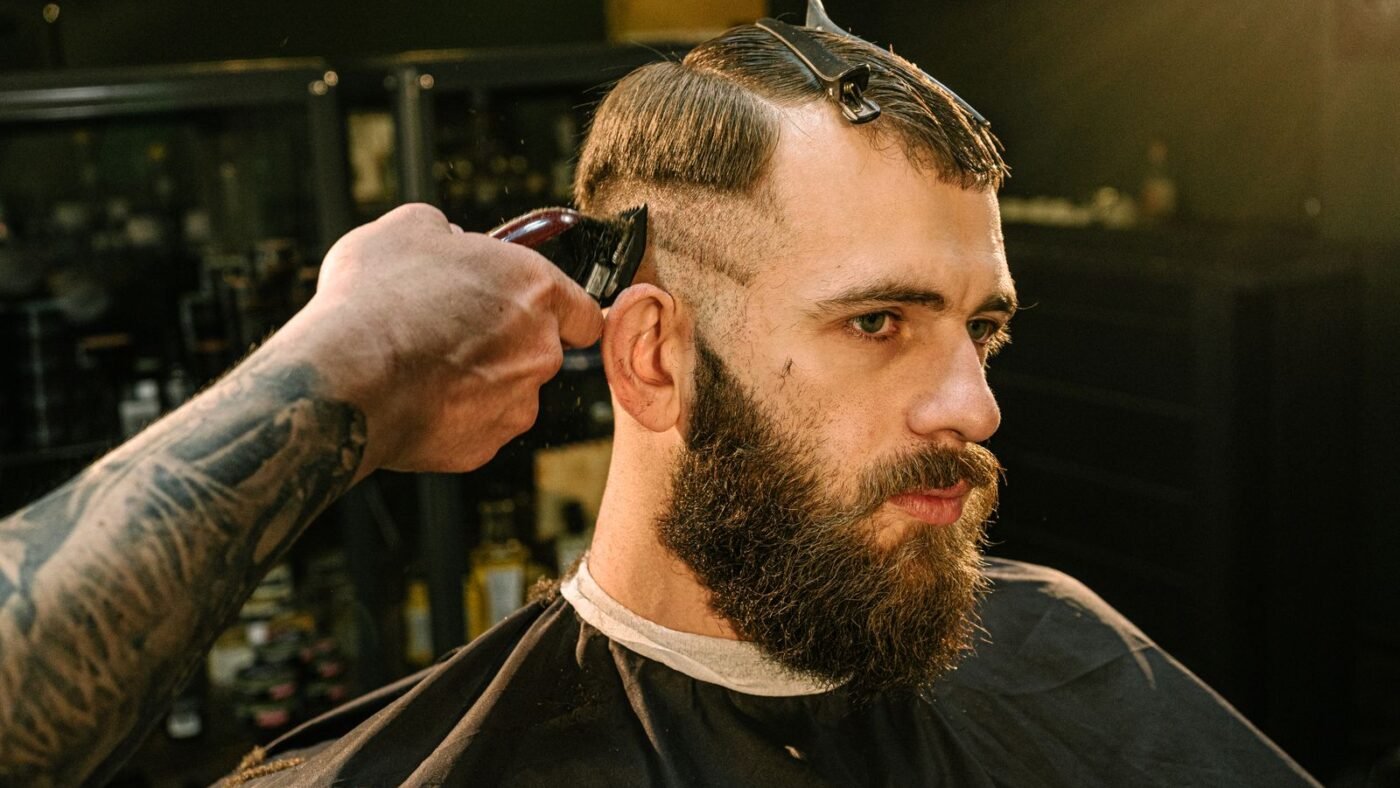 Barbeiro passando a máquina na lateral do cabelo de um cliente de barba na barbearia