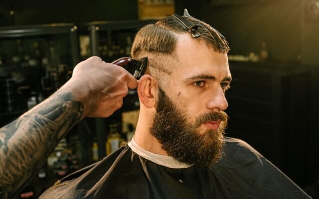 Barbeiro passando a máquina na lateral do cabelo de um cliente de barba na barbearia
