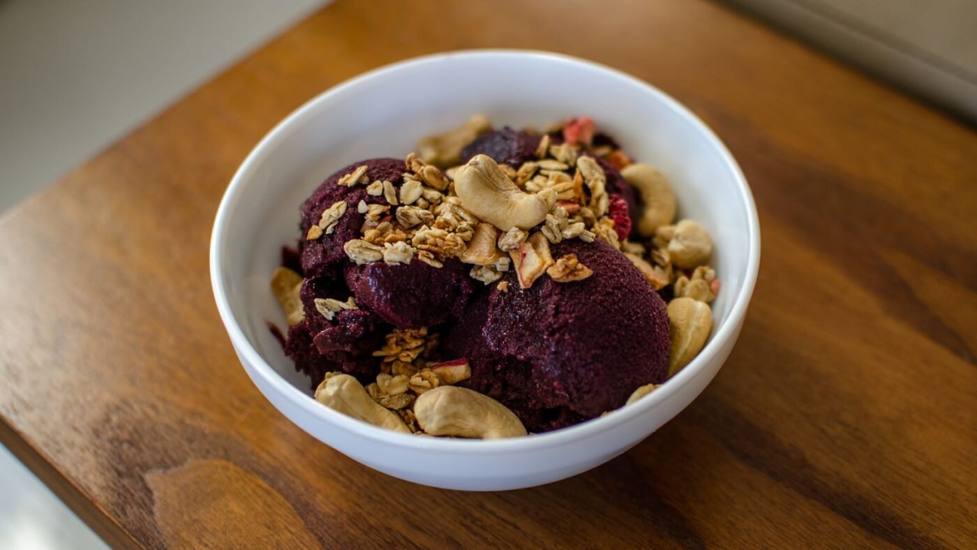 Tigela branca de açaí com granola e castanha de caju sobre mesa de madeira