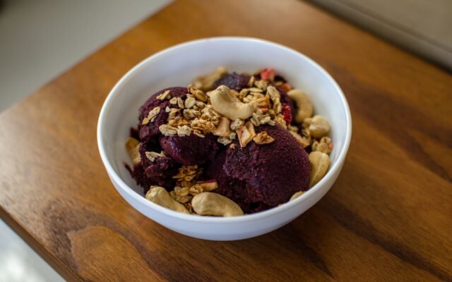Tigela branca de açaí com granola e castanha de caju sobre mesa de madeira