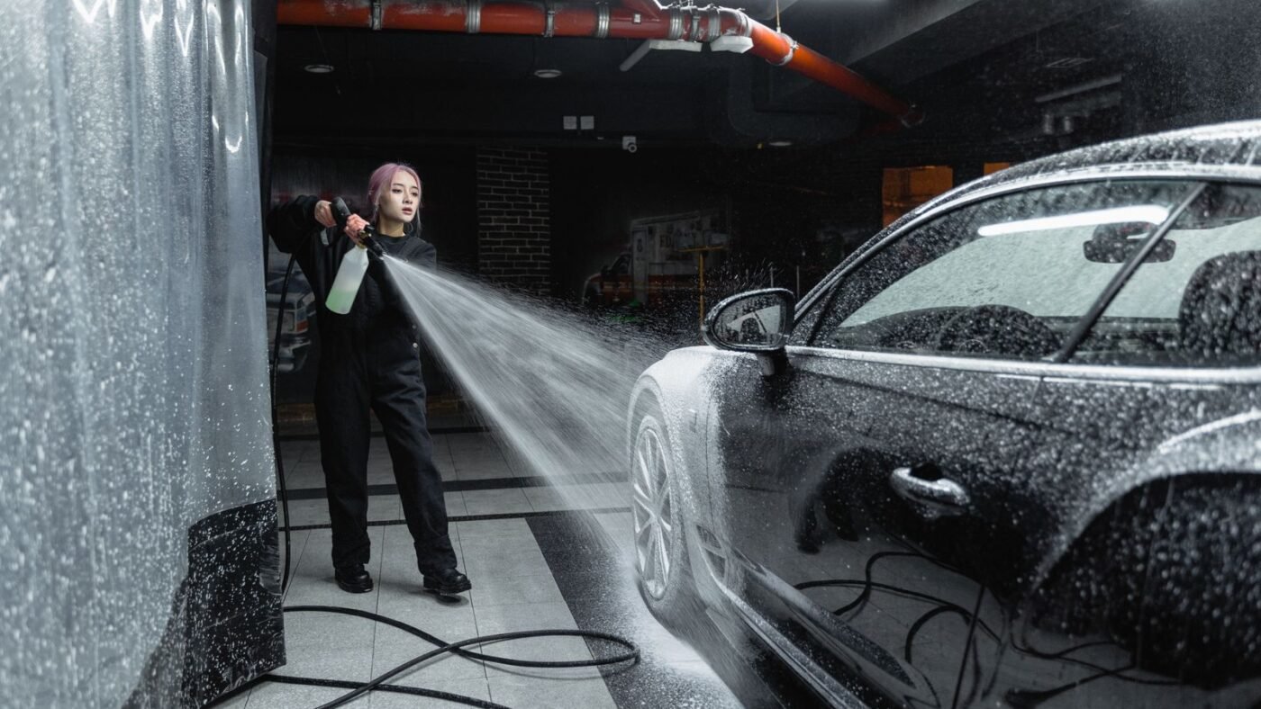 Funcionária de lava-rápido enxaguando carro com espuma usando lavadora de alta pressão