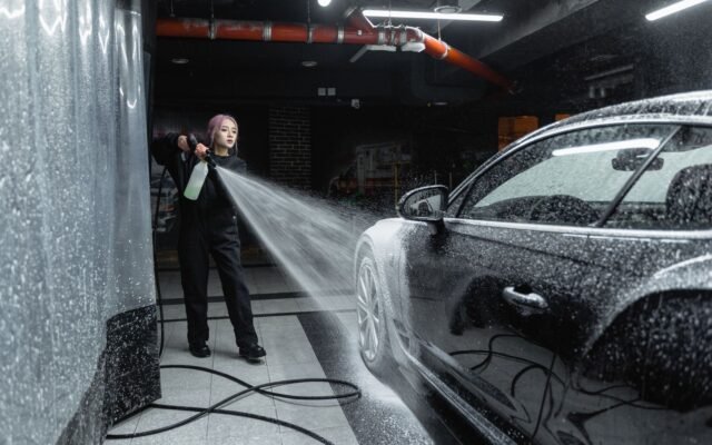 Funcionária de lava-rápido enxaguando carro com espuma usando lavadora de alta pressão