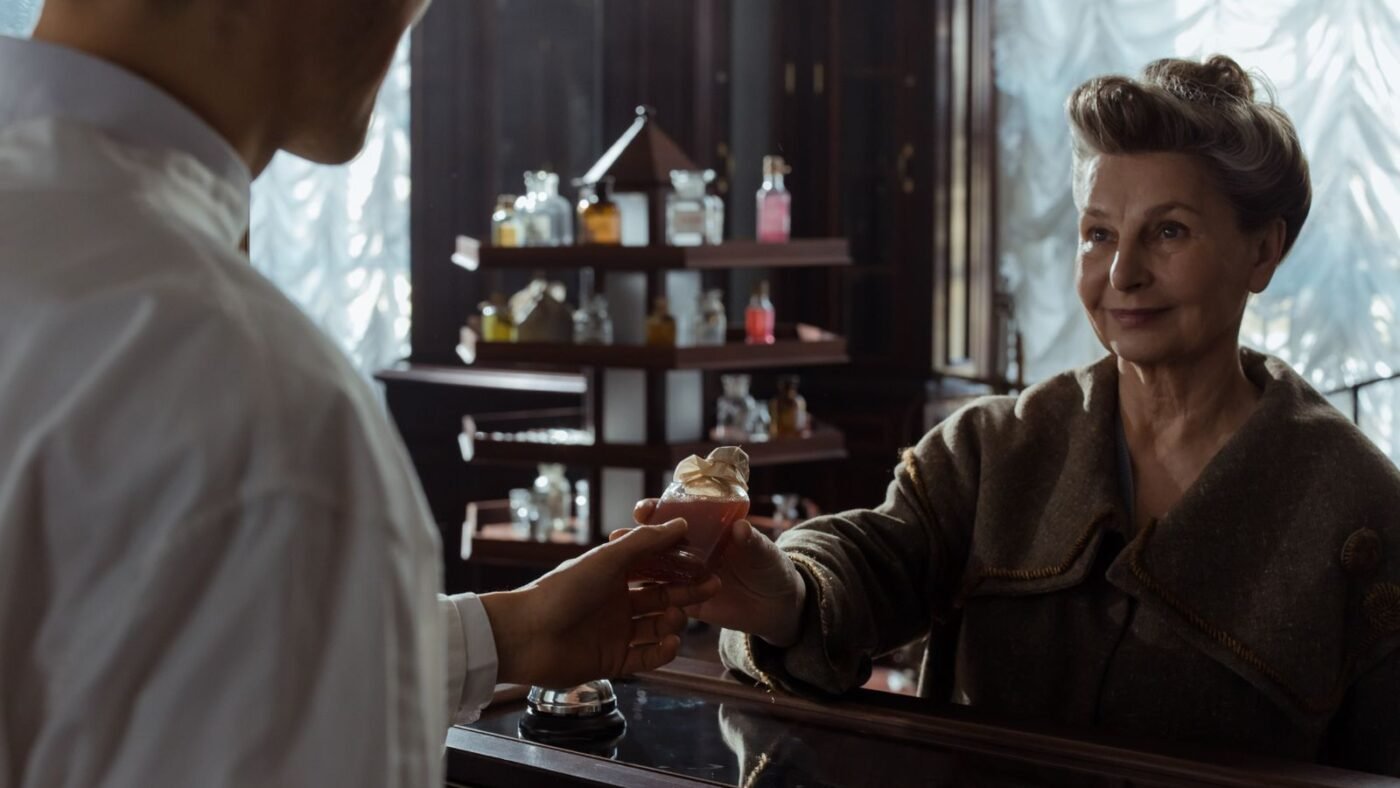 Atendente entregando frasco de perfume a uma cliente no balcão de uma perfumaria antiga