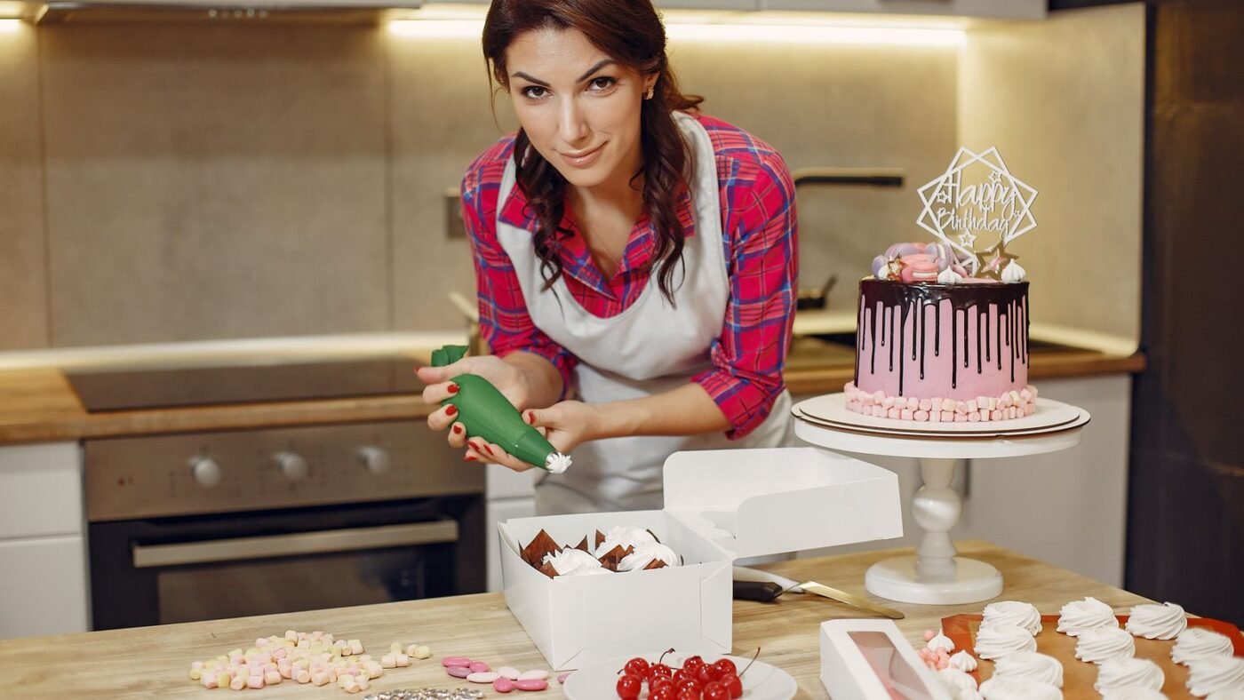Confeiteira decorando bolo de aniversário com cobertura de chocolate na cozinha de casa