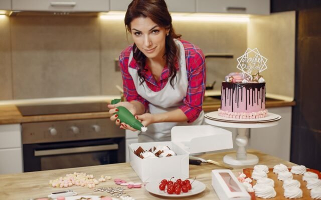 Confeiteira decorando bolo de aniversário com cobertura de chocolate na cozinha de casa