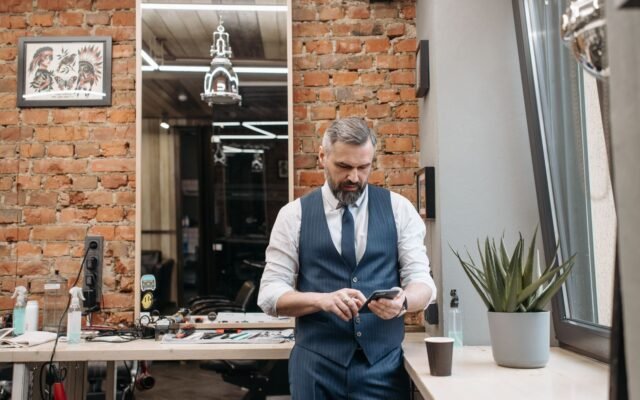 Dono de barbearia mexendo no celular encostado no balcão do salão