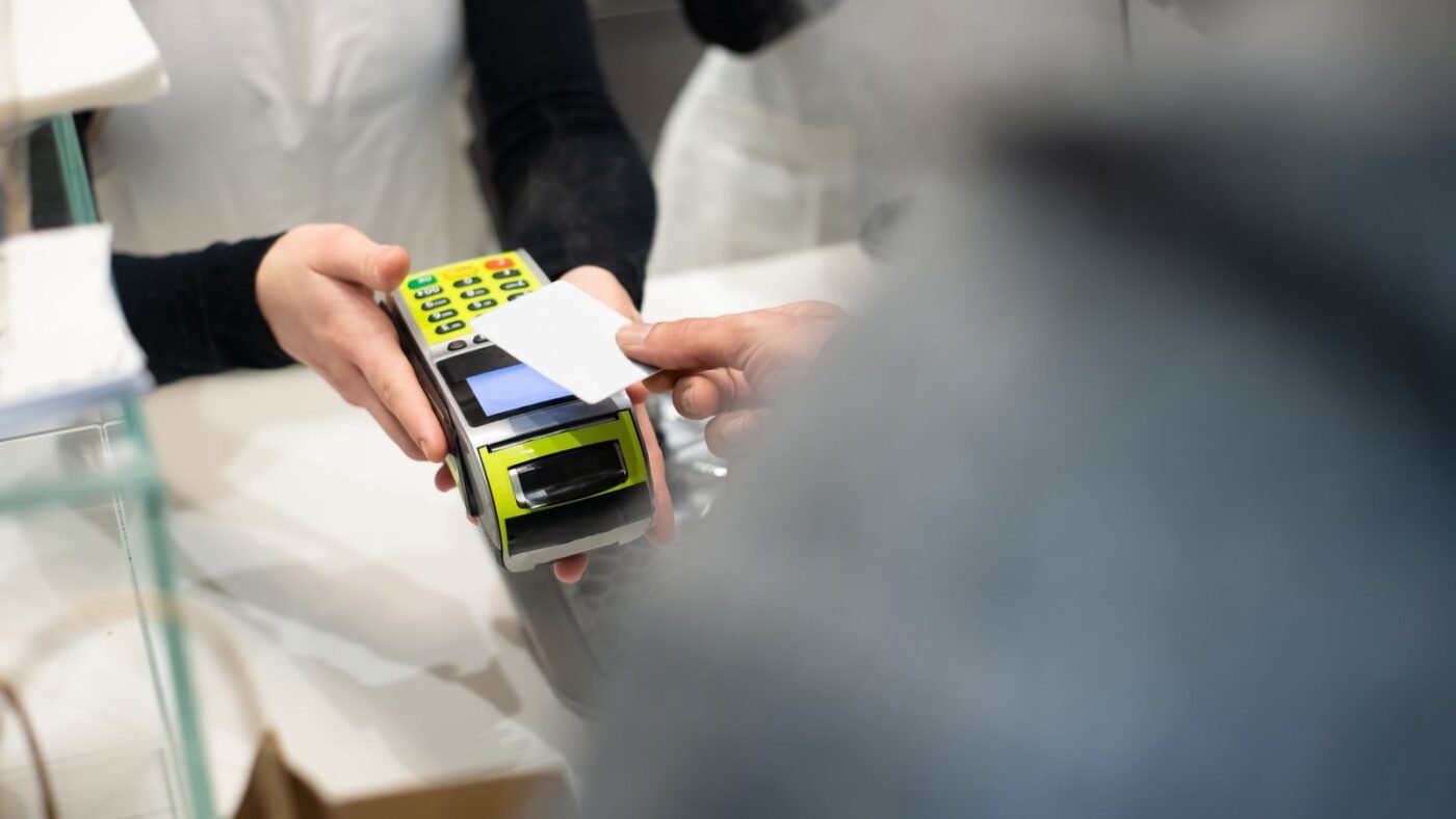 Cliente inserindo o cartão na maquininha segurada pela atendente no balcão da loja