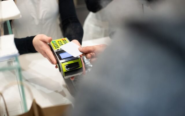 Cliente inserindo o cartão na maquininha segurada pela atendente no balcão da loja